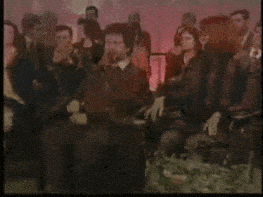 a group of people are sitting in front of a sign that says era un complotto