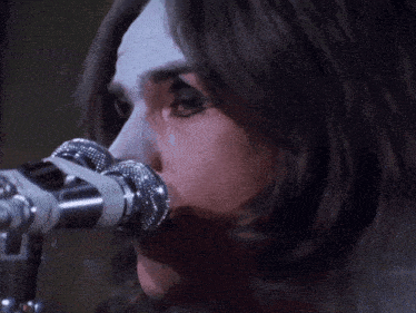a woman singing into a microphone with a white face paint