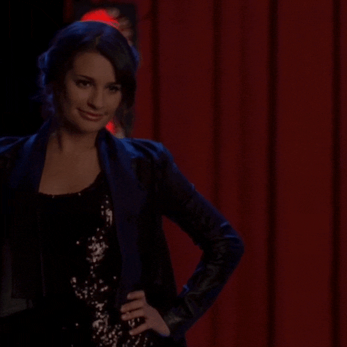 a woman in a black jacket stands in front of a red curtain with her hands on her hips