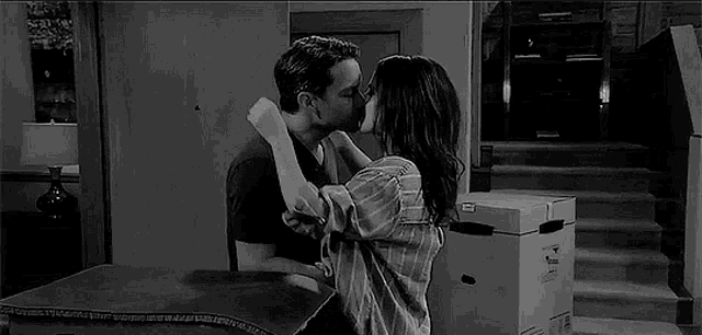 a black and white photo of a man and woman kissing in a room .