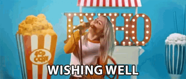 a woman is singing into a microphone in front of a popcorn cart and says wishing well .