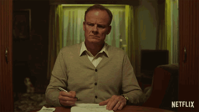 a man sits at a table with a pen in his hand and a netflix logo in the corner