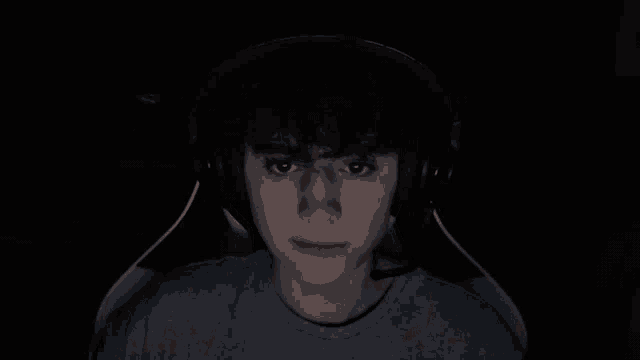 a man wearing headphones looks at the camera in the dark