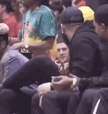 a man wearing a tie dye shirt sits in the stands with other people