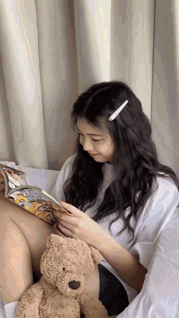 a woman is holding a teddy bear while reading a book