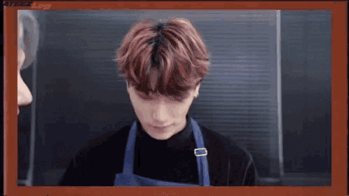 a young man with red hair and a blue apron is looking down .
