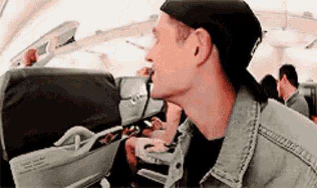 a man wearing a hat and a denim jacket is sitting on an airplane .