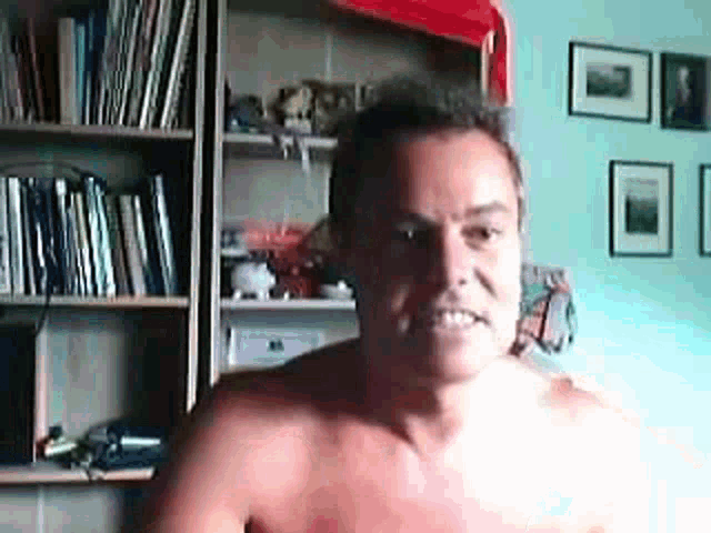 a man without a shirt is standing in front of a bookshelf in a room .