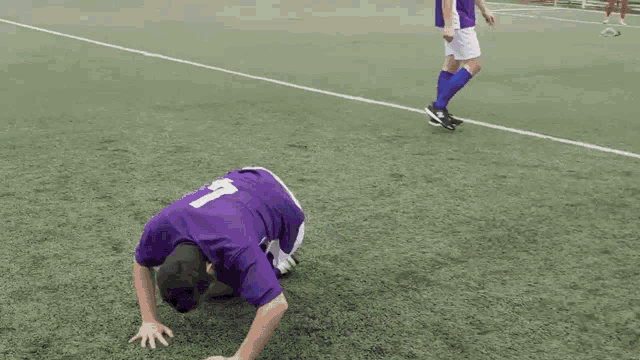 a man in a purple jersey with the number 7 on it does a handstand on a soccer field