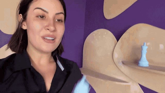 a woman in a black shirt is standing in front of a purple wall and a blue chess piece .