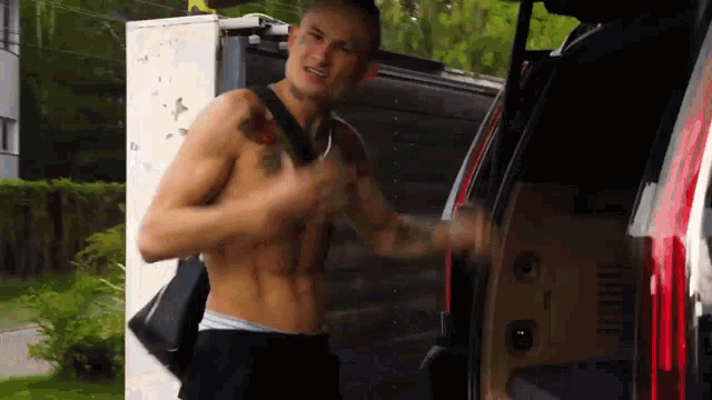 a shirtless man with a tattoo on his chest is standing in the back of a car .