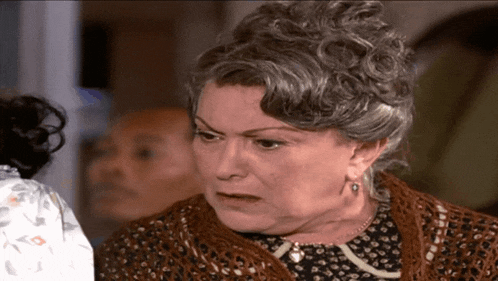 a woman with gray hair and a brown sweater looks angry
