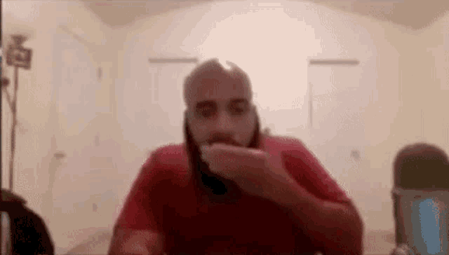 a man with a beard is sitting in front of a microphone in a room eating something .