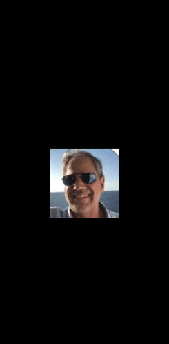 a man wearing sunglasses is smiling for the camera while standing in front of the ocean .