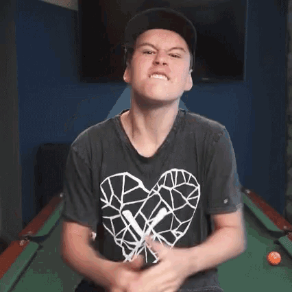 a young man wearing a black shirt with a heart on it is sitting in front of a pool table .