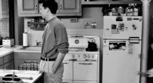 a man is standing in a kitchen in front of a refrigerator and stove .