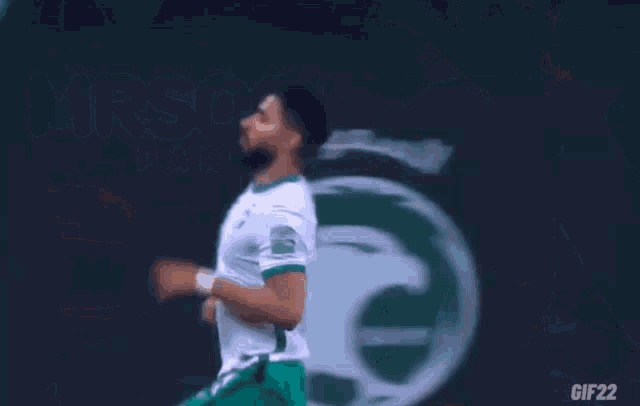 a soccer player in a white shirt and green shorts is being photographed by a cameraman