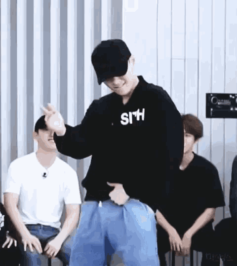 a man wearing a black hat and a black sweatshirt is dancing in front of a group of people sitting in chairs .