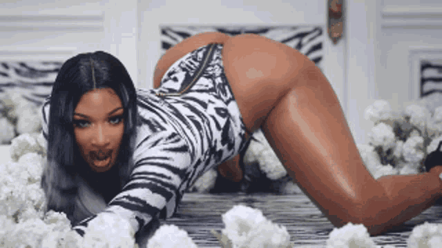 a woman in a zebra print bodysuit is kneeling on a bed of flowers