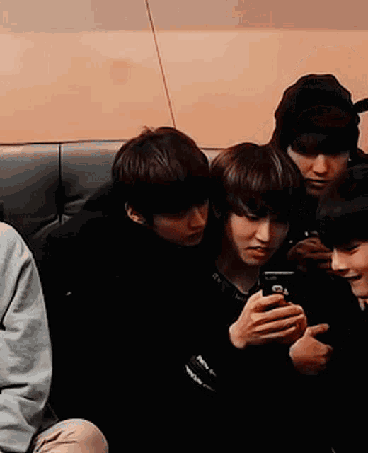 a group of boys are sitting on a couch looking at a cell phone