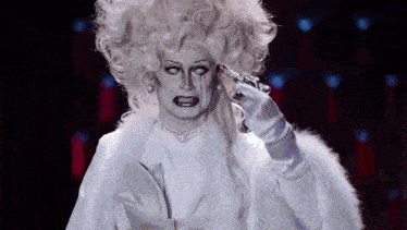 a woman in a white wig and gloves is holding a gun to her head