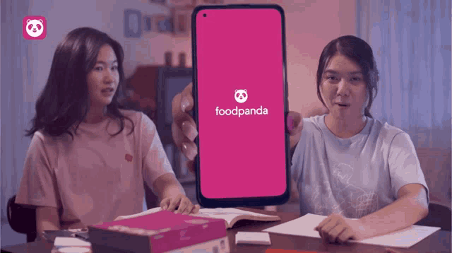 two girls sitting at a table with a phone that says foodpanda