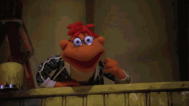 a muppet with glasses and red hair is standing on a balcony holding something .