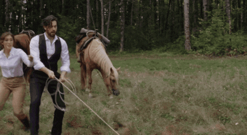 a man and a woman are pulling two horses through a field