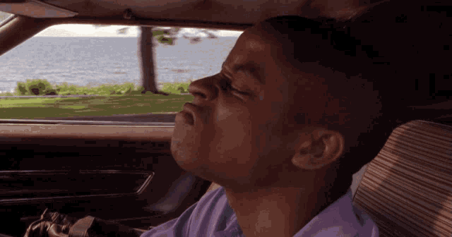 a man in a purple shirt is yawning in the back seat of a car