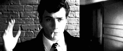a man is smoking a cigarette in front of a brick wall .