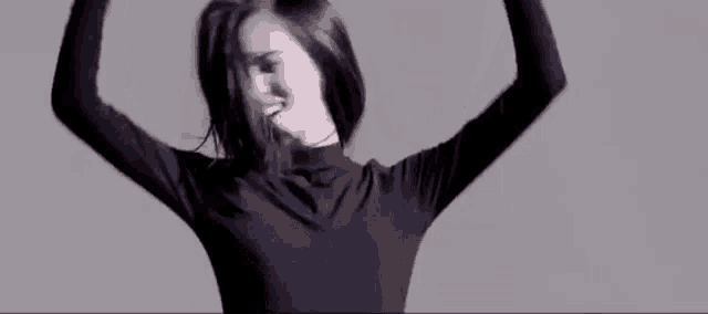 a woman in a black turtleneck is dancing with her hands in the air .
