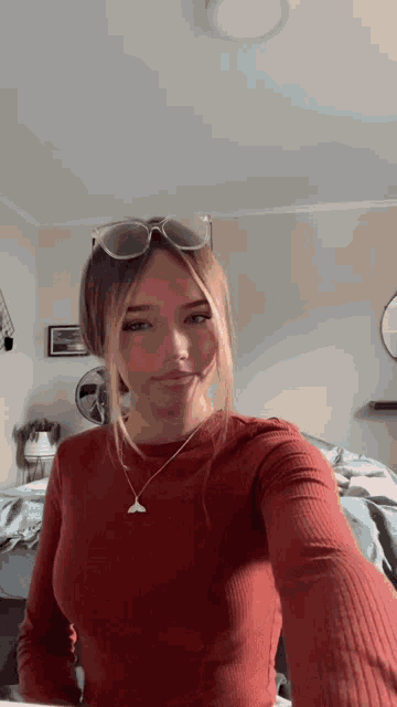 a woman wearing sunglasses and a necklace takes a selfie in a bedroom