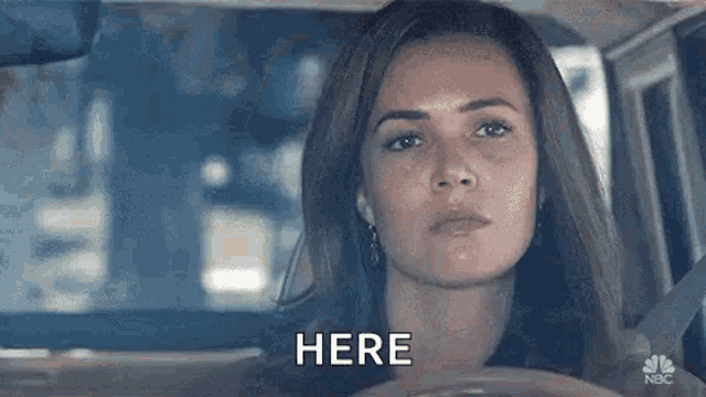 a woman is sitting in the driver 's seat of a car and says `` here '' .