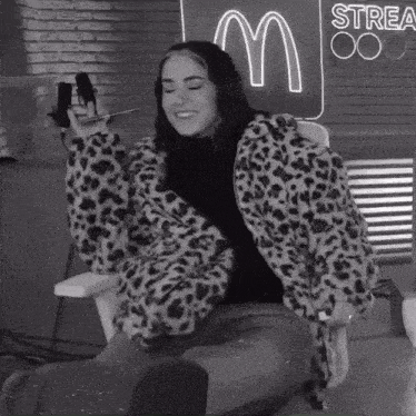 a woman in a leopard print jacket is sitting in front of a neon sign that says strea