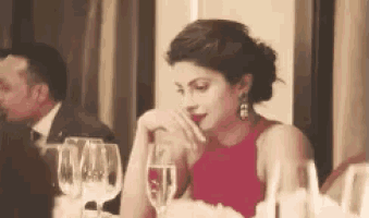 a woman in a red dress is sitting at a table holding a glass of wine .