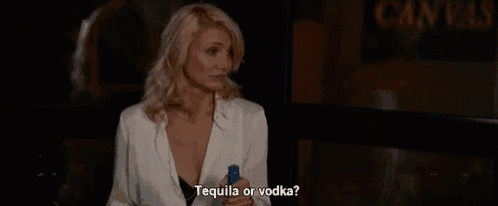 a woman is sitting at a table holding a bottle of tequila and a shot glass .