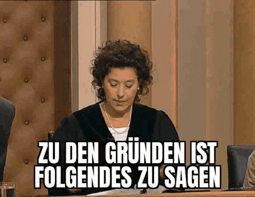 a woman is sitting at a table with a sign that says zu den grunden ist folgendes zu sagen .