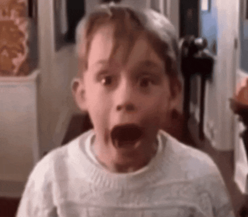 a young boy is making a surprised face while wearing a white sweater