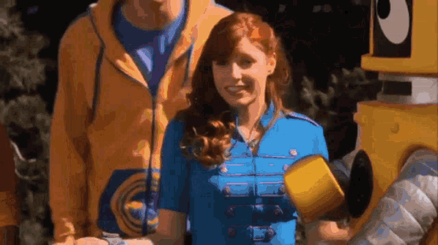 a woman in a blue uniform is smiling in front of a yellow robot