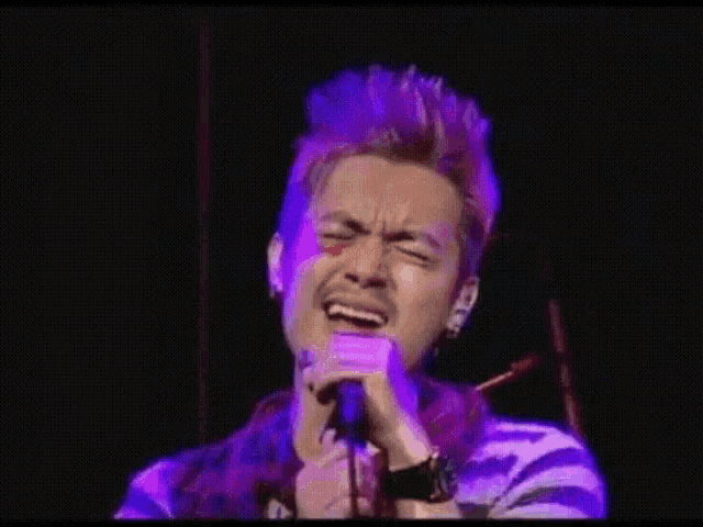 a man with purple hair singing into a microphone