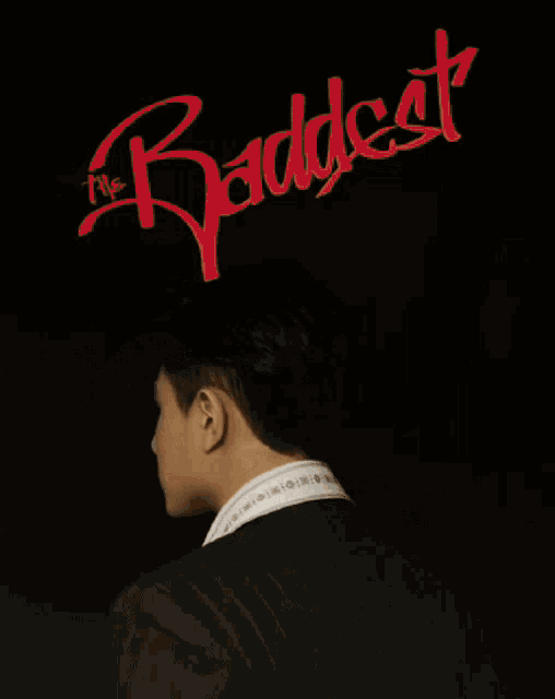 a man in a suit stands in front of a poster that says " the baddest "