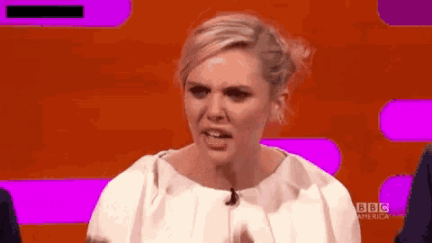 a woman in a white dress is making a funny face while sitting on a stage .