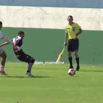 a soccer player kicks the ball while a referee stands behind him
