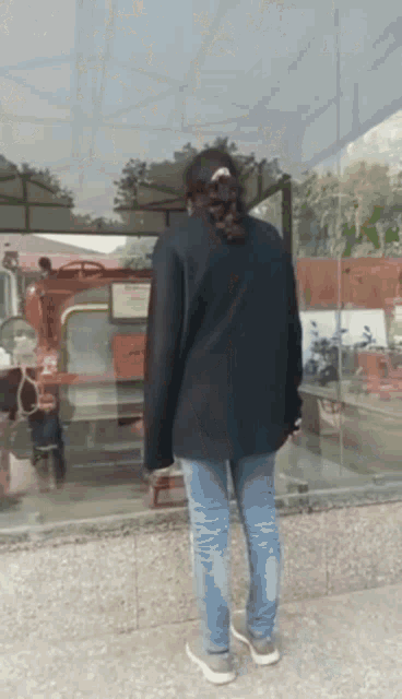 a person standing in front of a bus stop with a reflection of a bus in the glass
