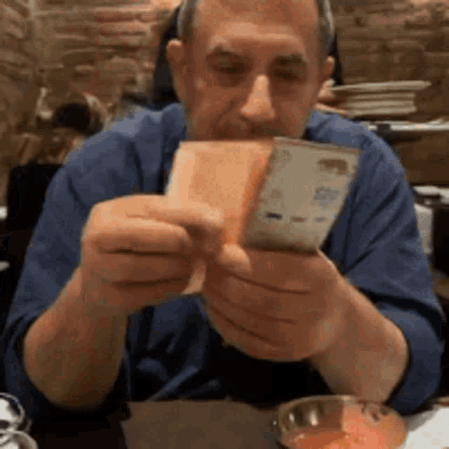 a man in a blue shirt is holding a piece of bread and a piece of money in his hands