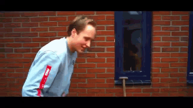 a man standing in front of a brick wall with a blue window