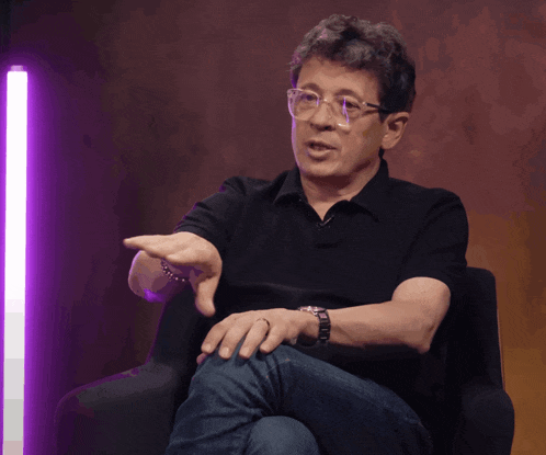 a man wearing glasses is sitting in a chair and pointing