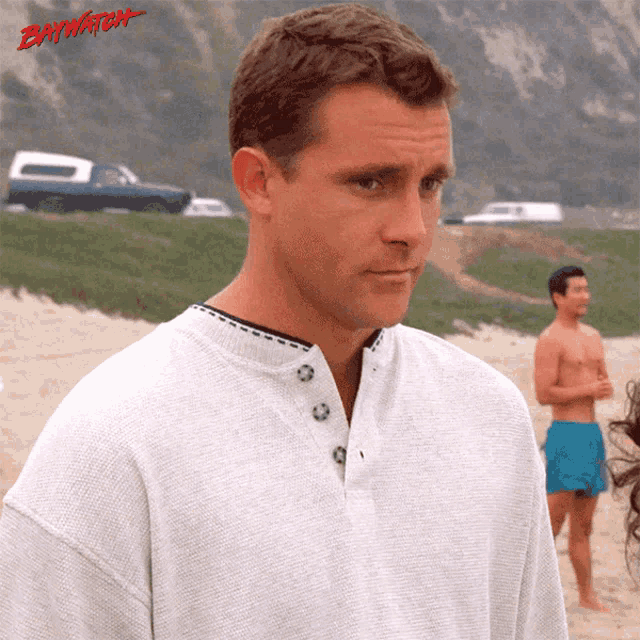 a man standing on a beach with the word baywatch on the bottom right