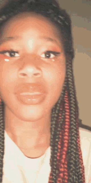 a close up of a woman 's face with braids and a white shirt