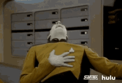 a man in a yellow uniform is holding his chest with his hands .